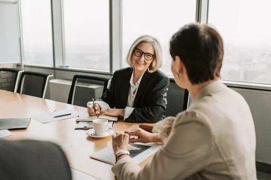 Manager kijkt naar de medewerker met een glimlach terwijl zij aan het noteren is tijdens een functioneringsgesprek