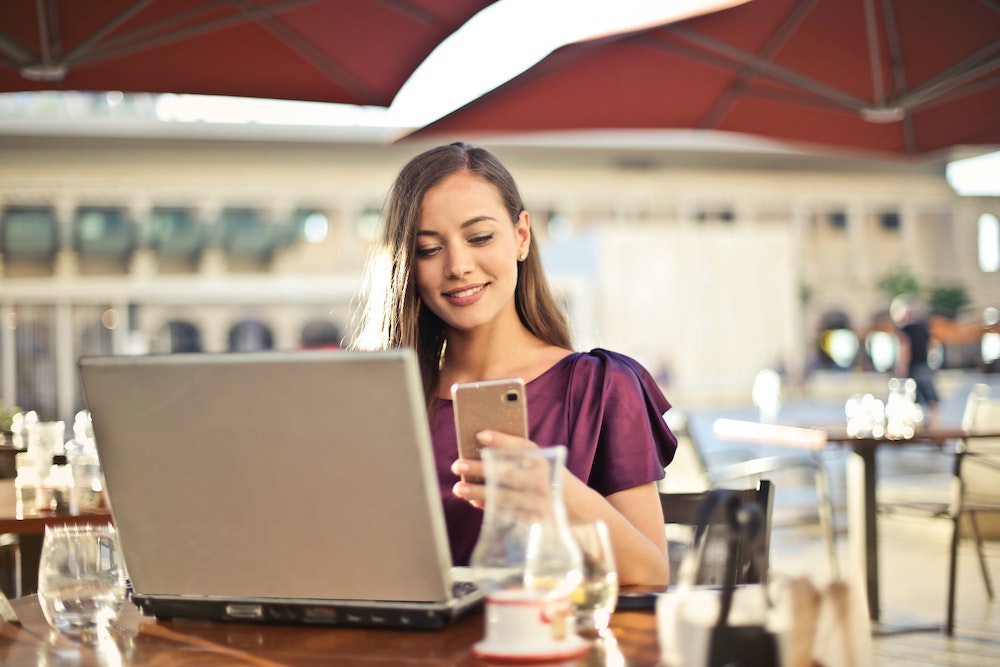 Vrouw aan het werk achter laptop kijkt even op telefoon